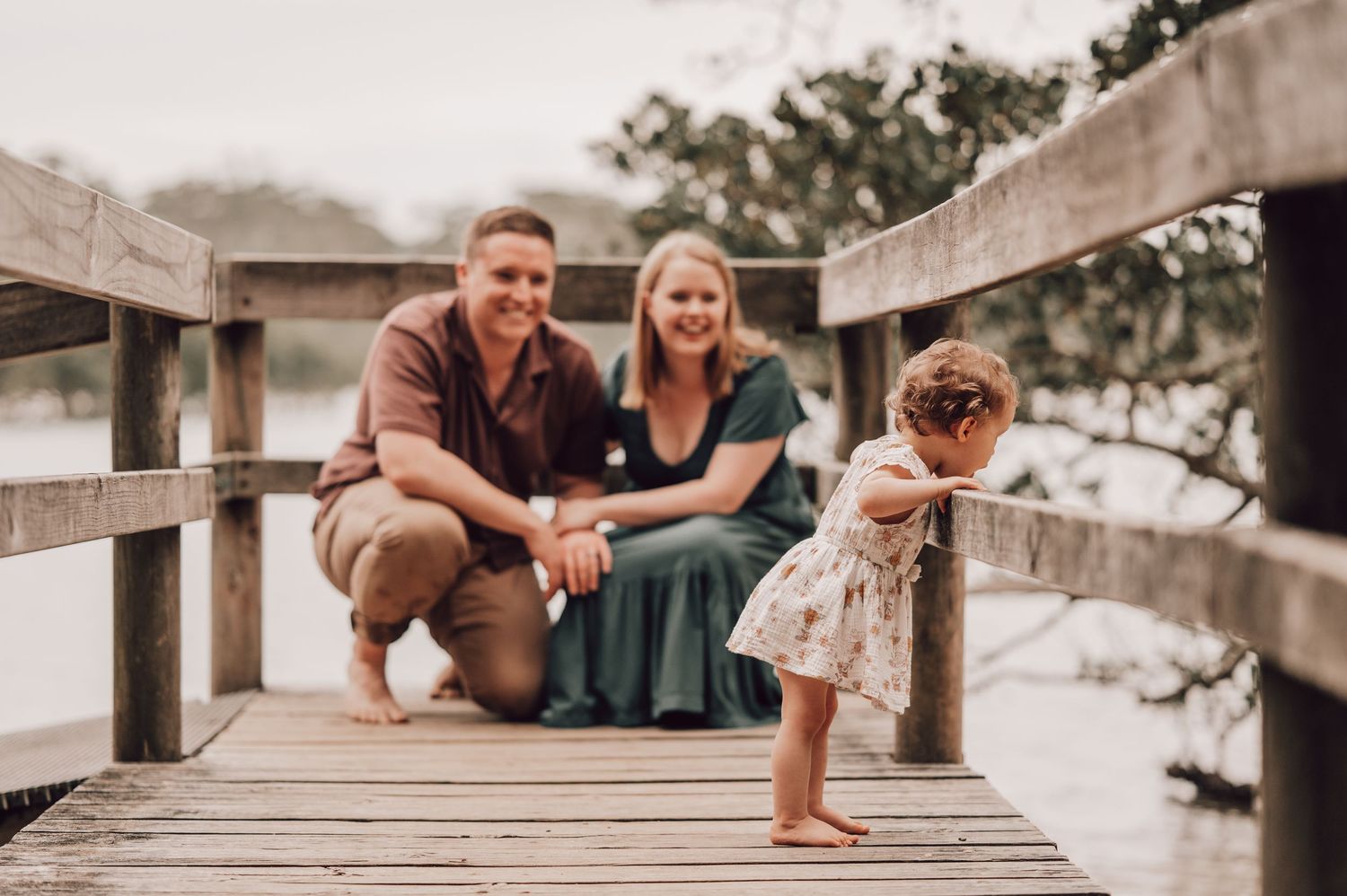 Happy family with toddler posing on wooden dock bridge near calm waterway. Family Photography