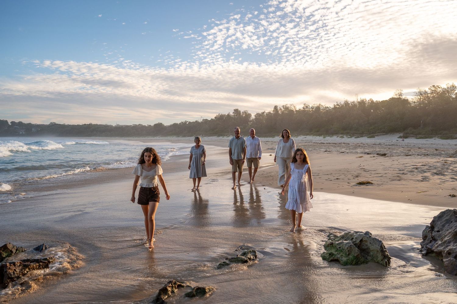 Family walking on a scenic beach at golden hour with waves and lush trees in the background. Family Photography