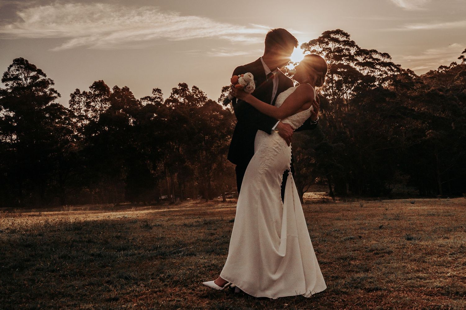 Wedding couple embracing at golden sunset in open field, romantic outdoor ceremony portrait. Wedding. Wedding Photography