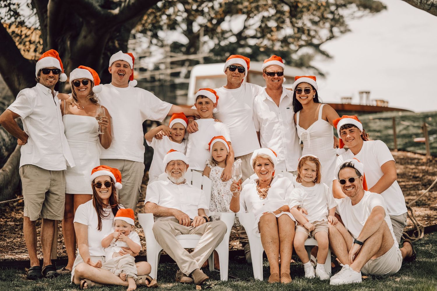Large family group in matching white outfits and Santa hats posing outdoors for a festive Christmas photo. Family Photography