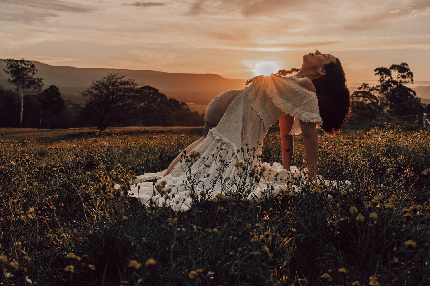 A woman in a white floral dress poses in a wildflower field at golden sunset with mountains in the background.
Maternity Photography