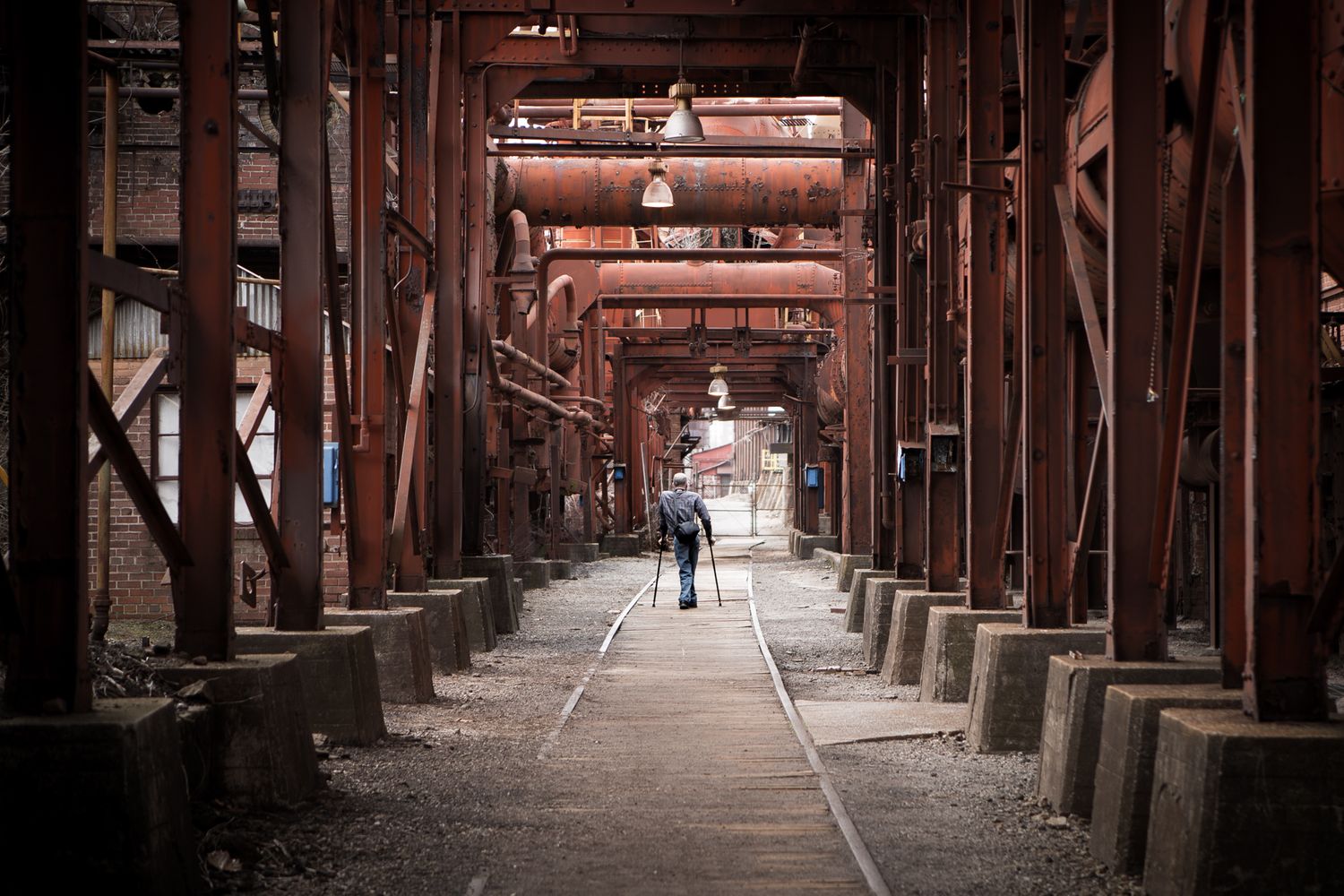 A man using crutches walks amid steel girders at an iron mill