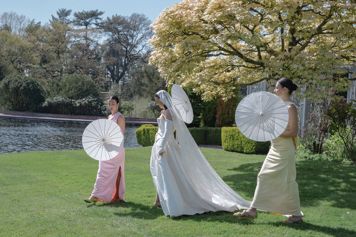 Bride  and bridesmaids walking the grounds of Capesthorne Hall with sun parasol and long veil - editorial wedding photographer Cheshire