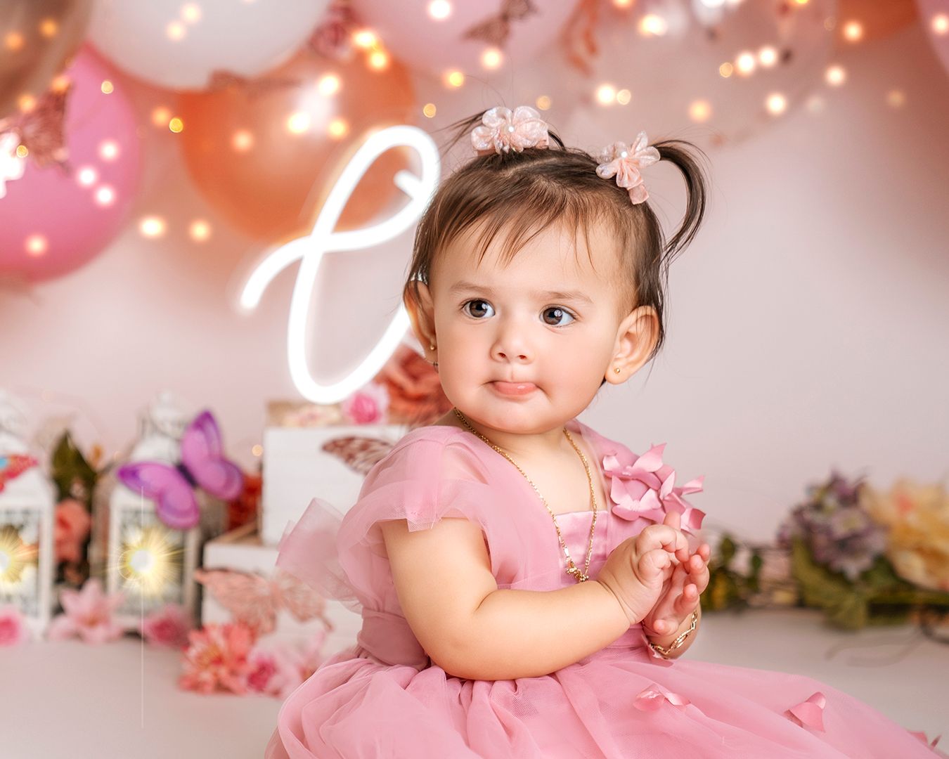 Baby wearing pink princess dress with balloon arch and floral backdrop.
