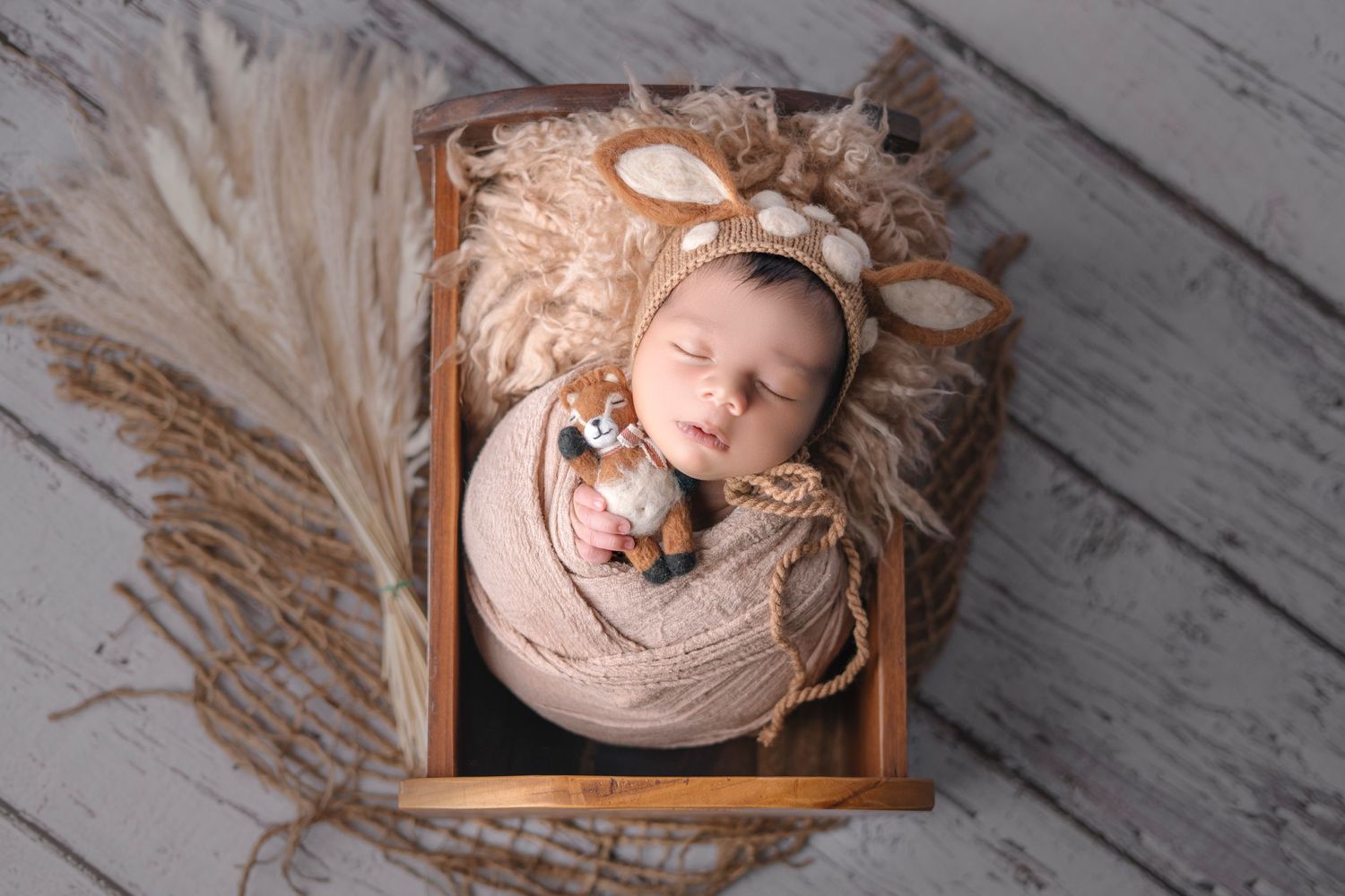 Newborn sleeping peacefully in wooden crate with bear bonnet and soft fur blanket.