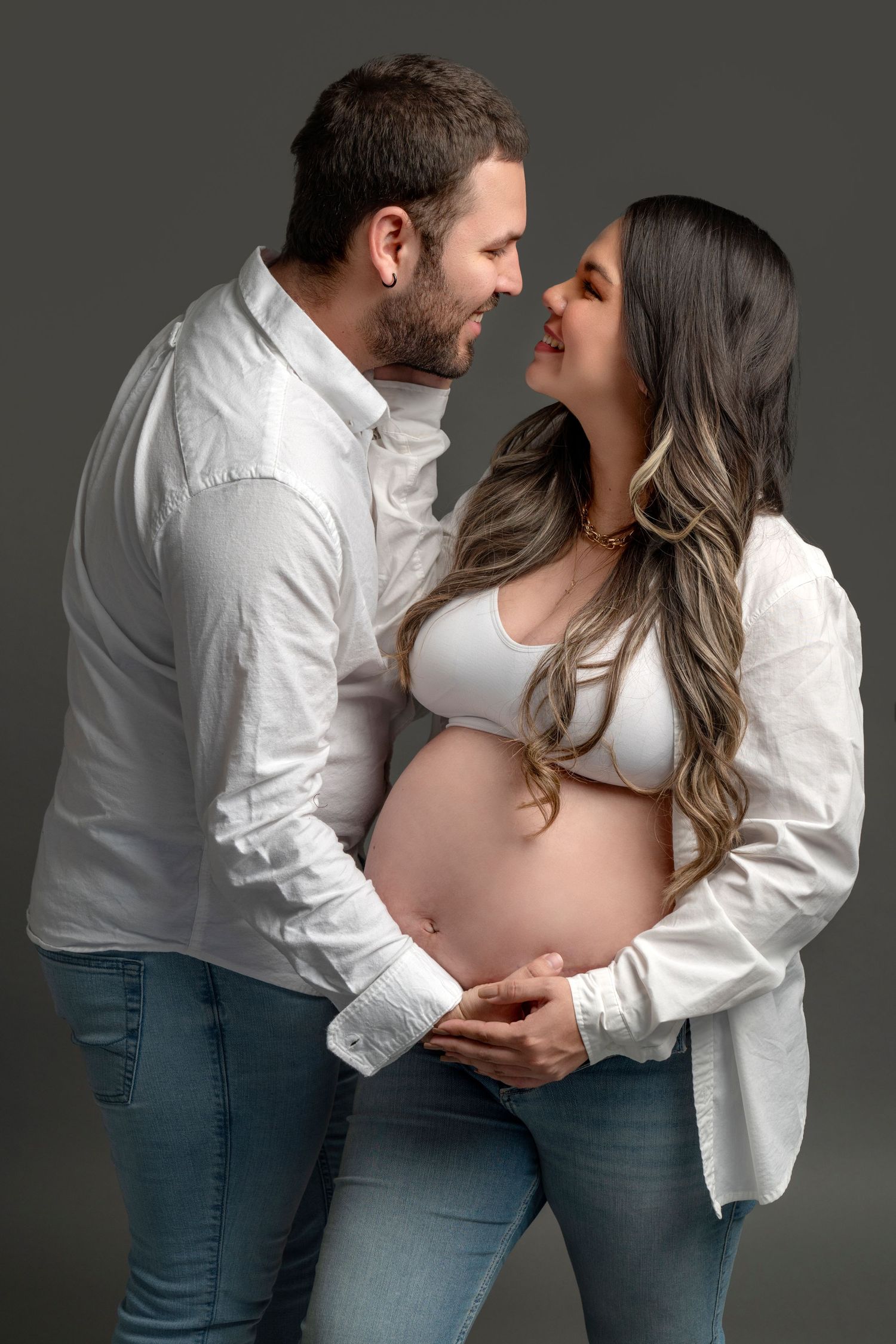 Intimate maternity portrait of couple in white shirts against dark background.
