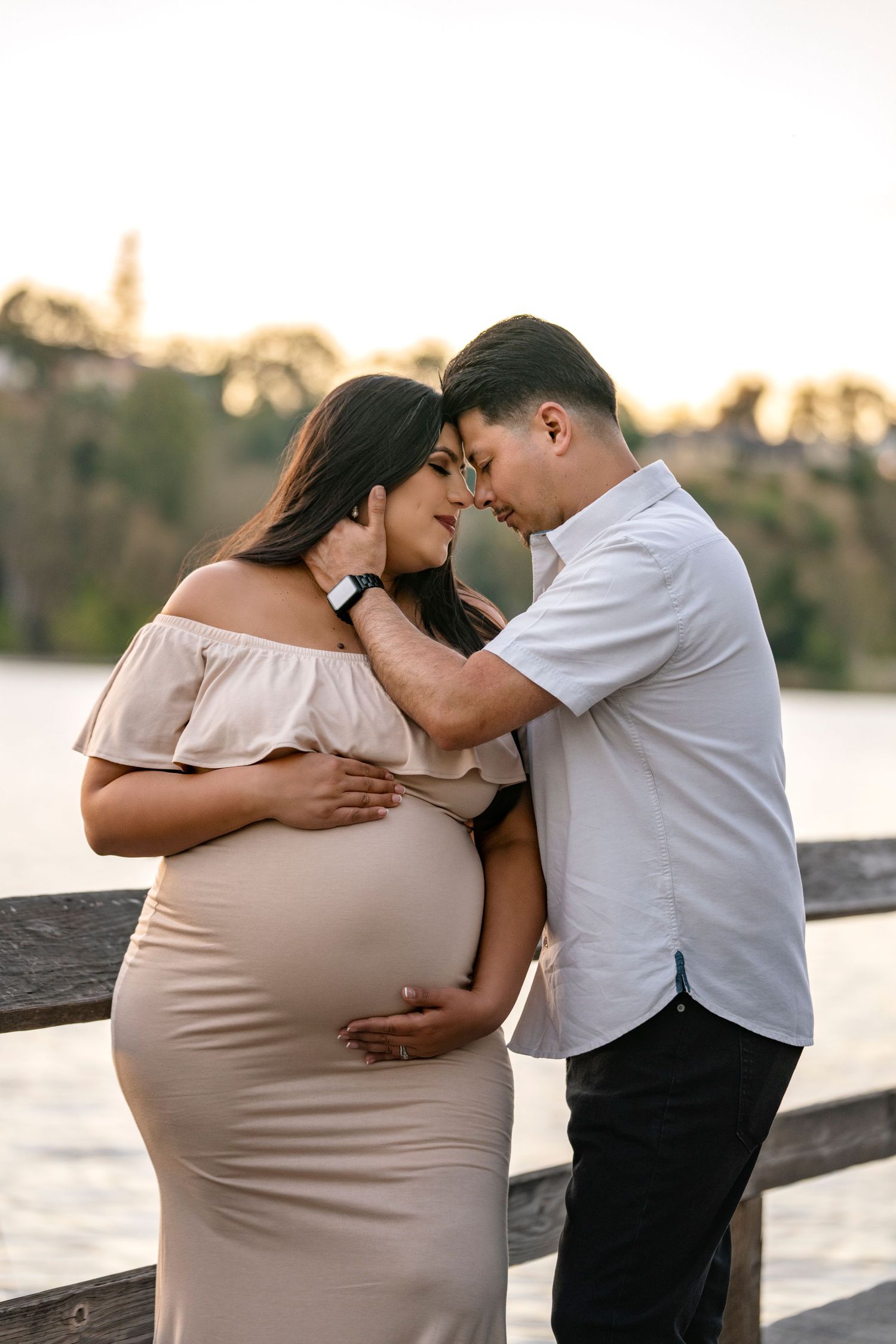 Tender maternity moment of couple by waterfront during sunset.