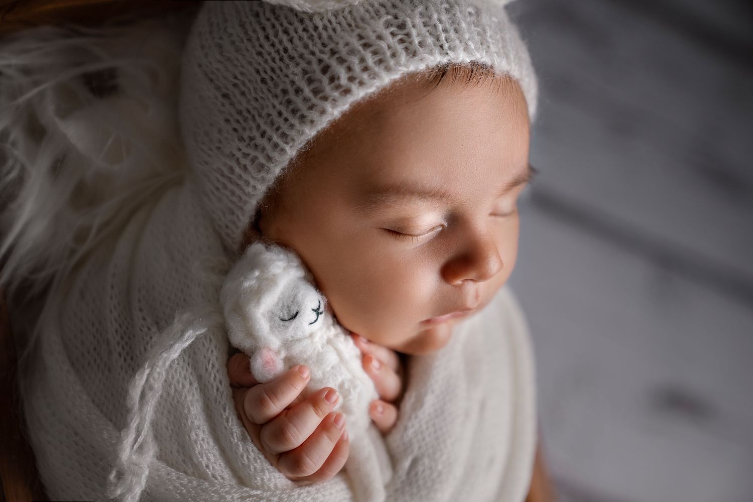 Close-up portrait of infant in white knit hat holding small plush toy, family photography near me, newborn photography