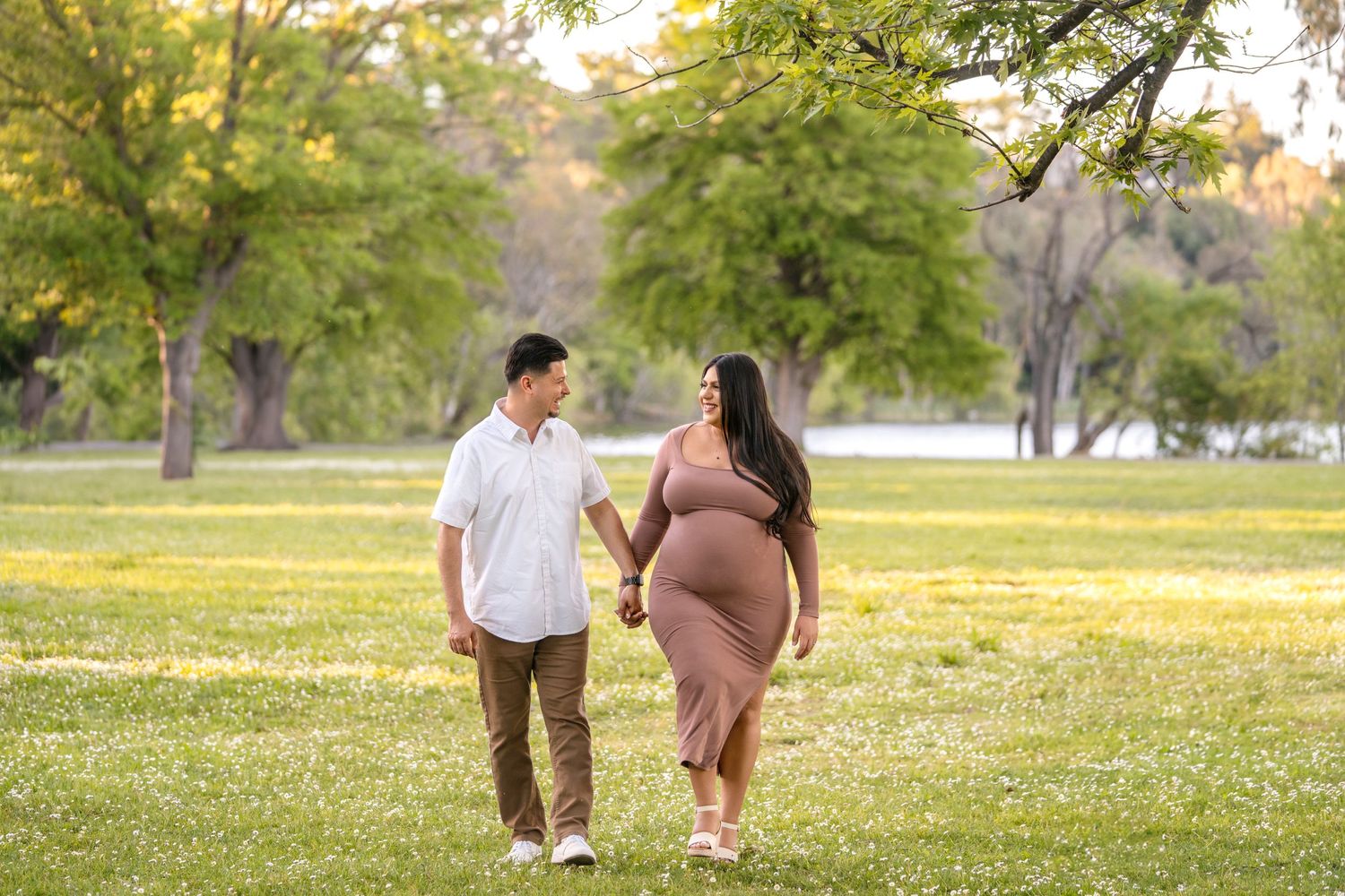 Couple walking hand in hand through a sunny park during golden hour.