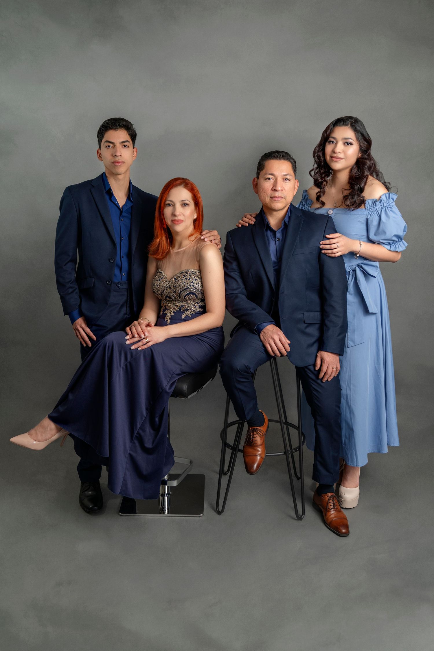 Formal family portrait with four people in blue and navy outfits against grey background.