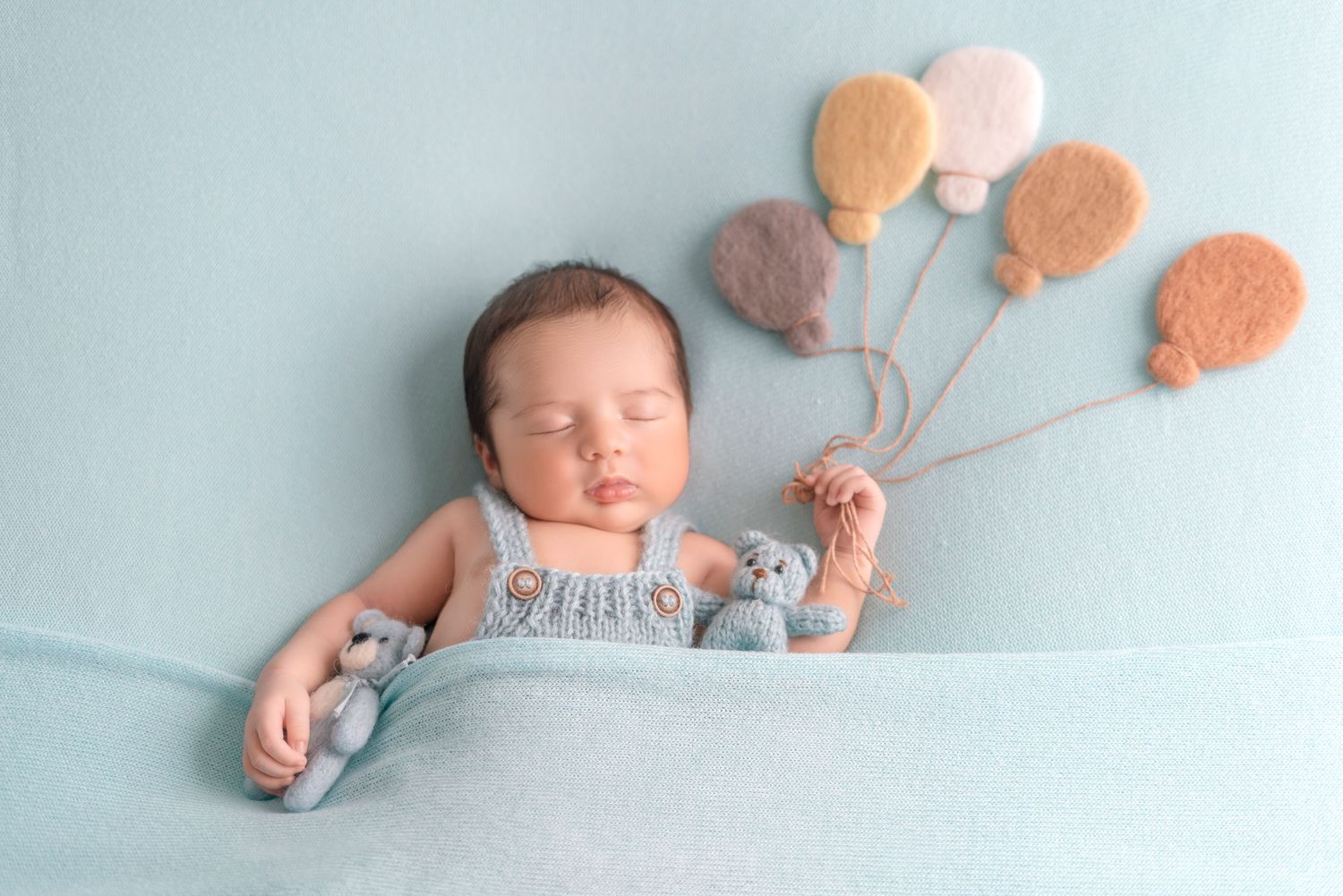 Sweet newborn scene with knit balloons and tiny teddy bears on blue backdrop.
