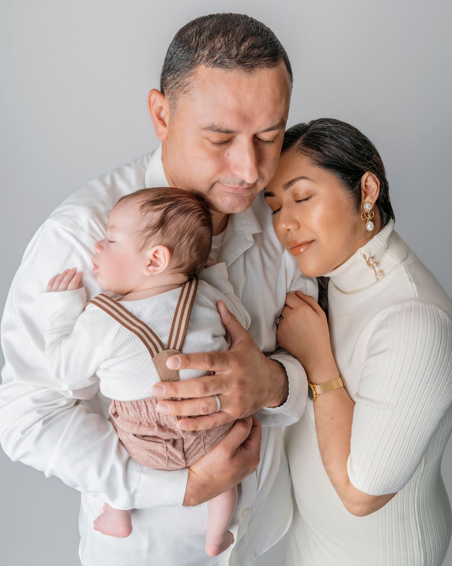 Intimate family portrait in white outfits against grey backdrop.