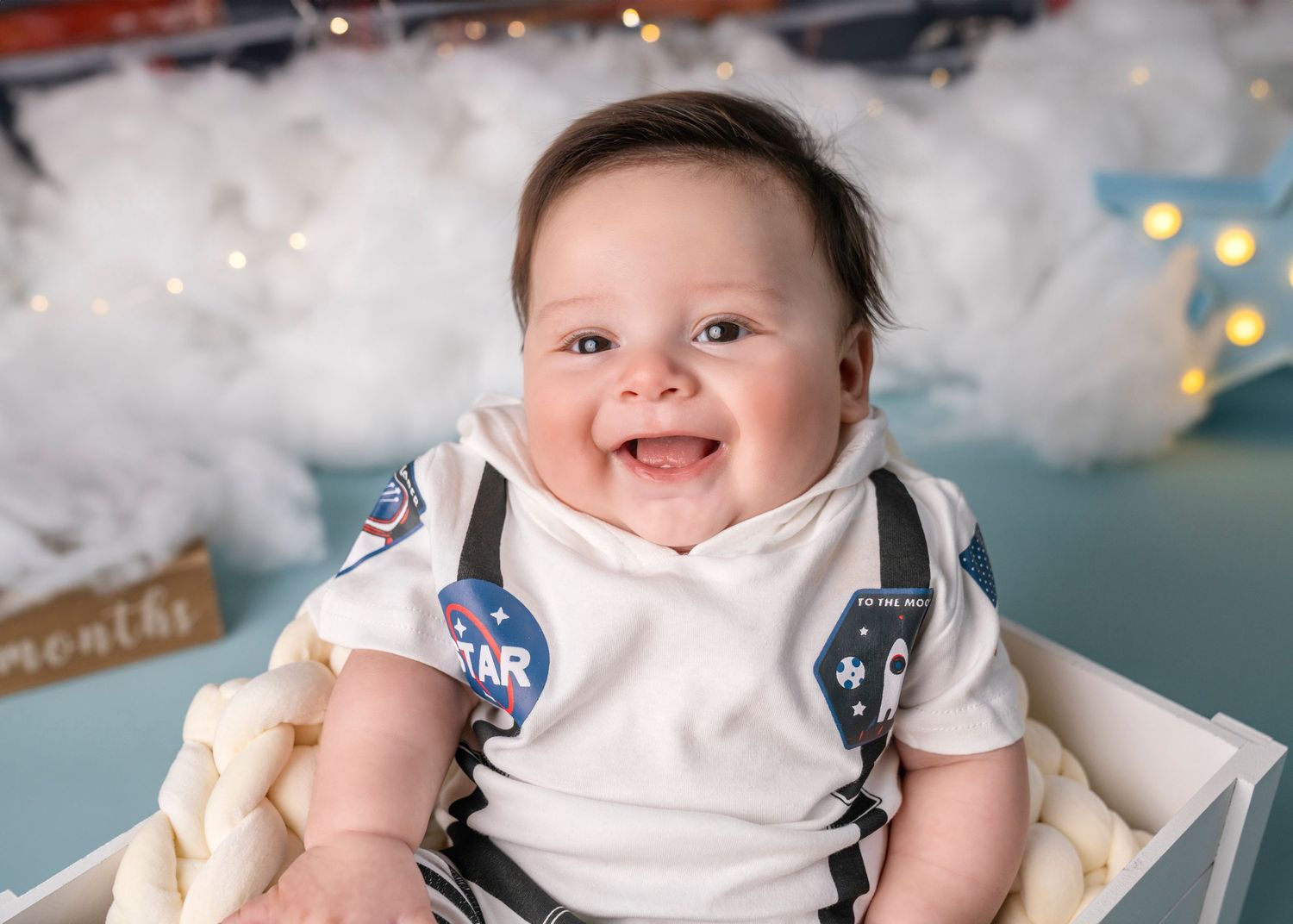 Happy baby wearing white onesie with suspenders smiles during professional photo session.