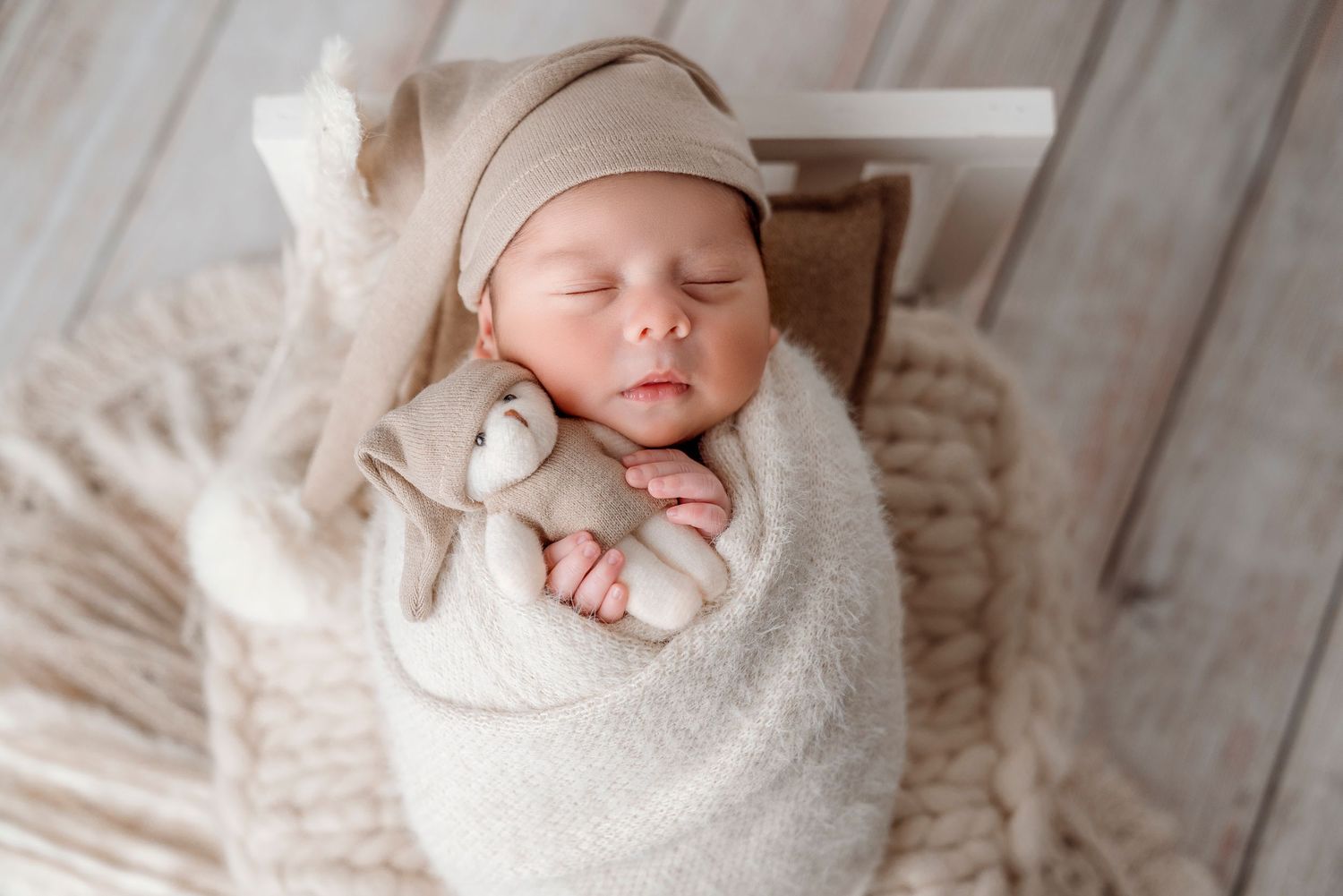 Sleeping newborn baby wrapped in white blanket holding small plush toy, newborn family photography, newborn baby photography