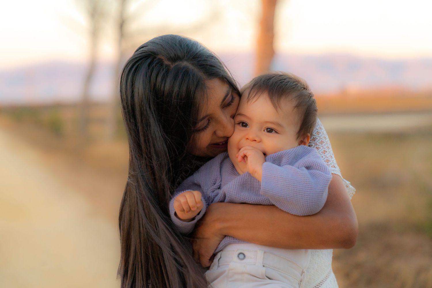 Tender moment captured at sunset with baby in blue sweater.