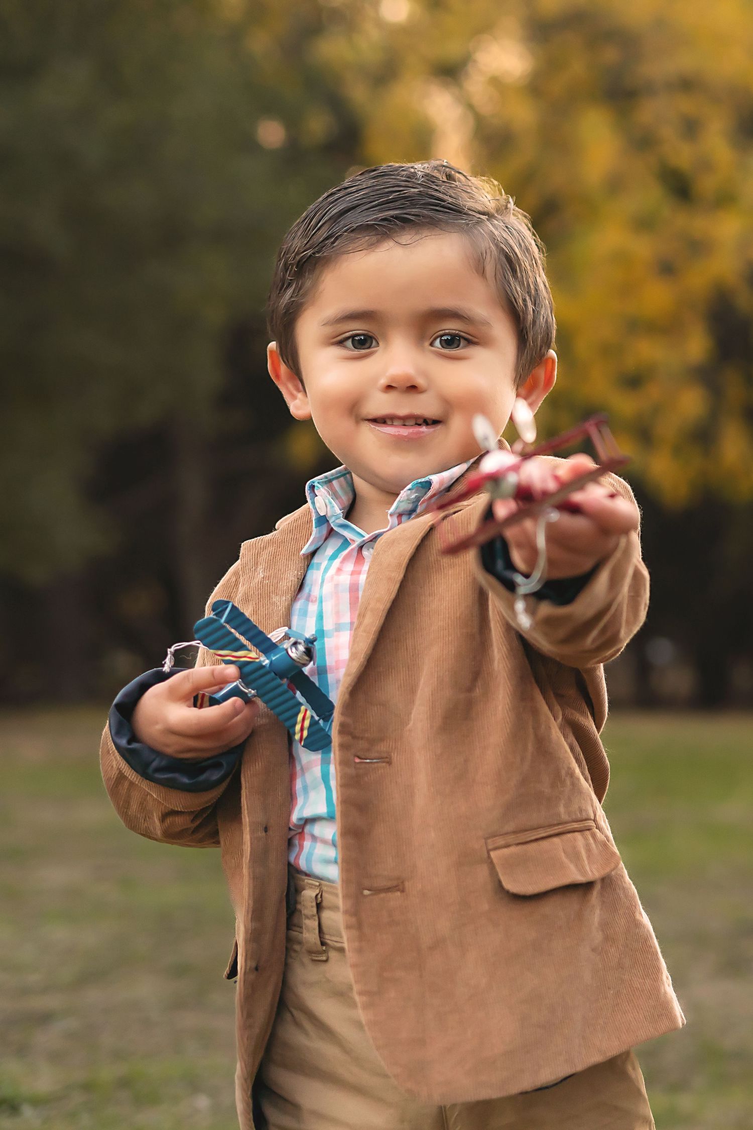 A child in a brown blazer and plaid shirt plays outdoors in autumn.