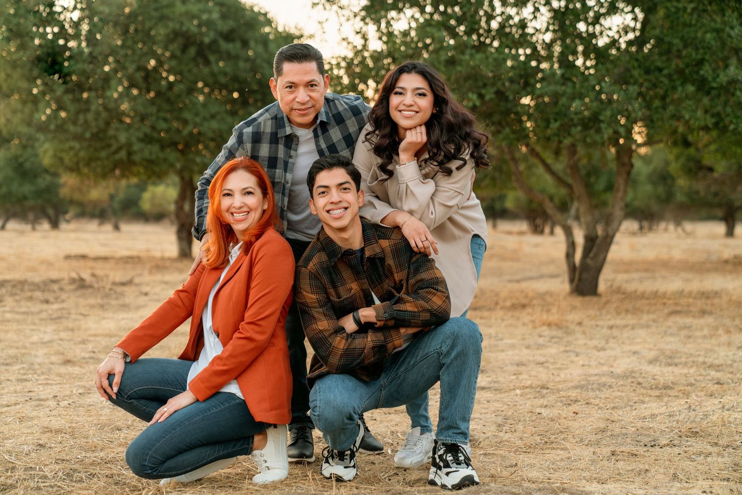 Group posing together in casual outfits on a grassy field during golden hour.
