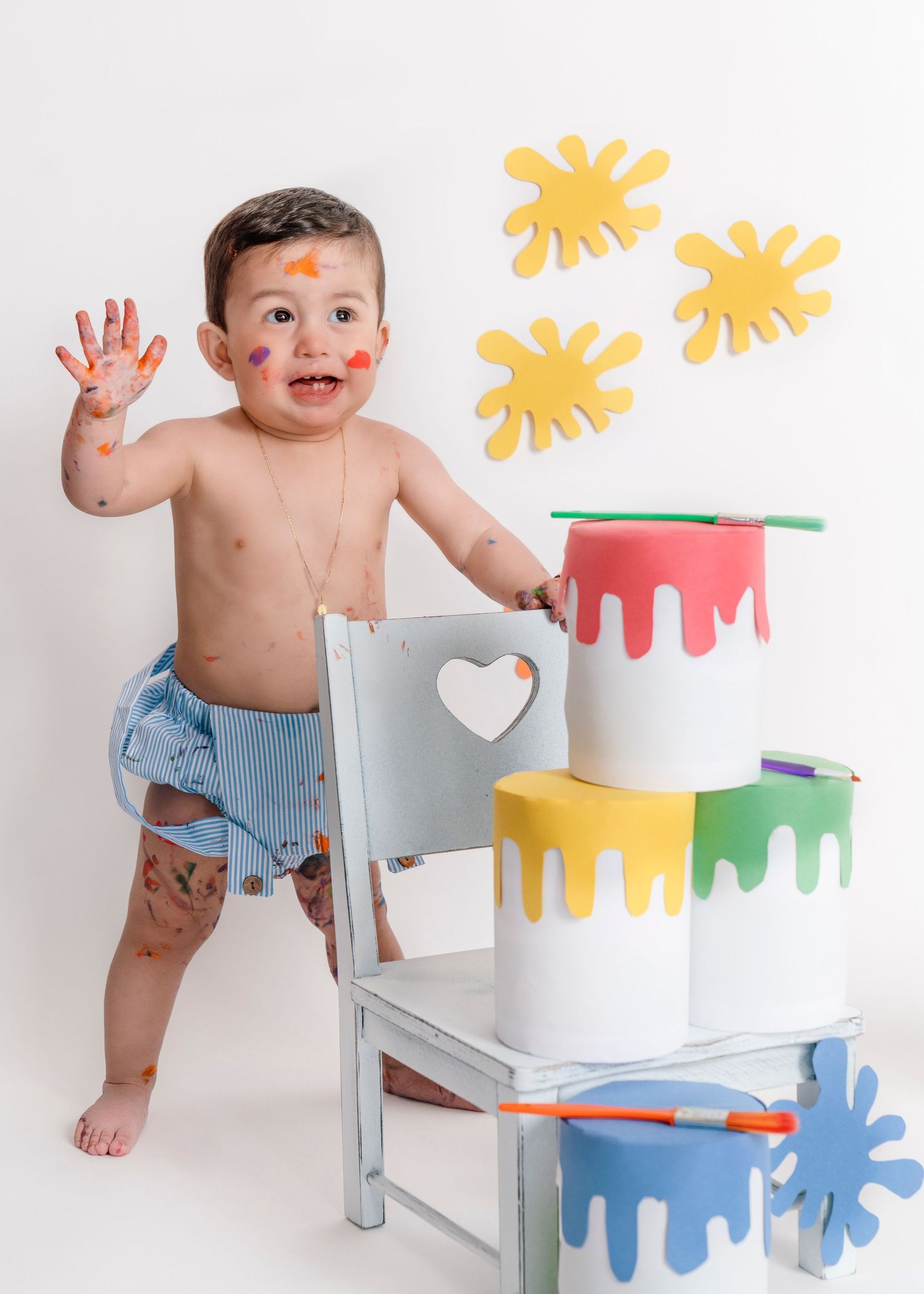 Paint-themed photoshoot with colorful drip decorations and baby in striped shorts.