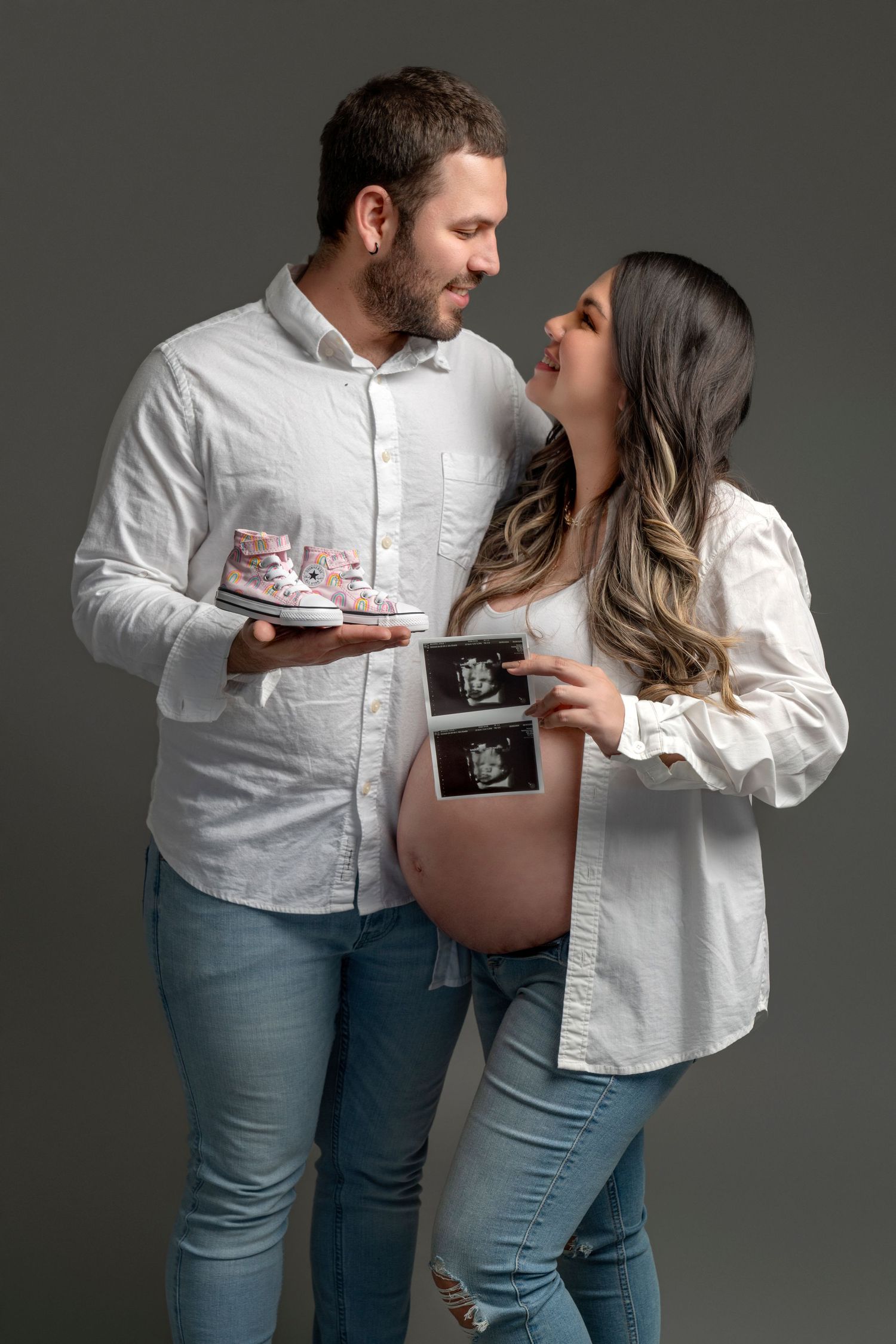 Couple sharing tender moment while holding ultrasound photos and baby shoes.