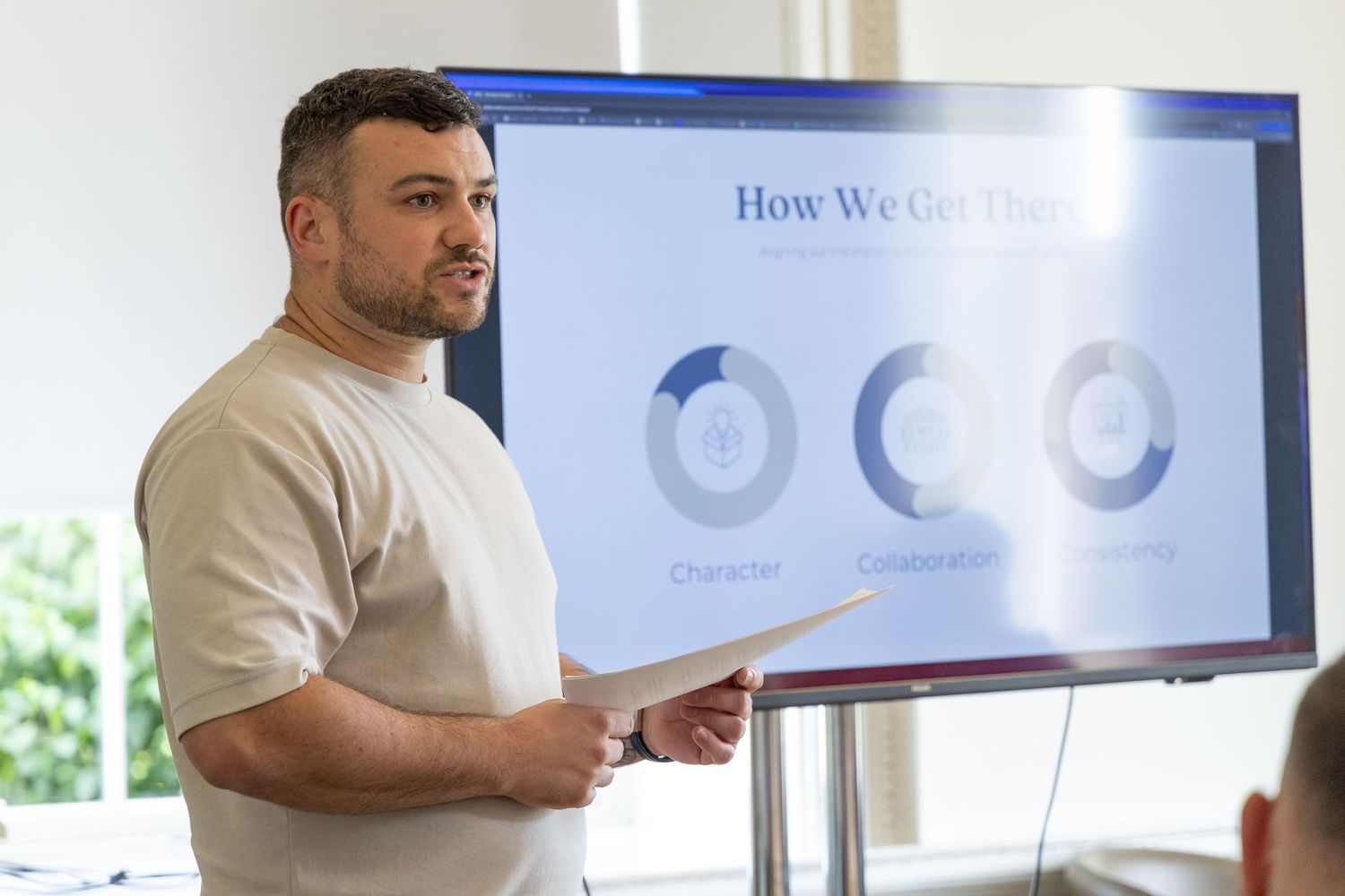 A person gestures while presenting data charts displayed on a large blue screen during a business presentation.
