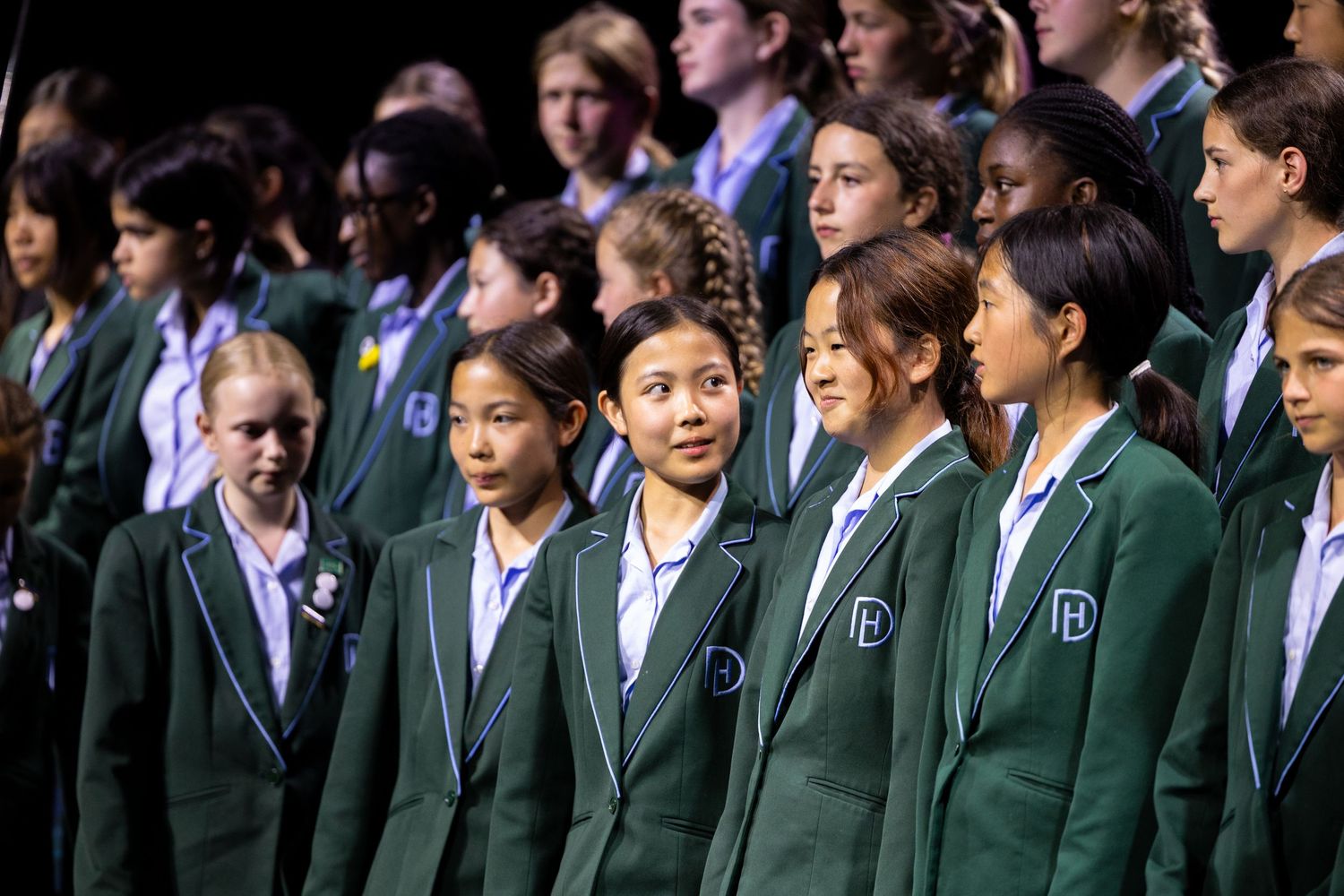 Students in green blazer uniforms stand together in formation during a school choir performance.