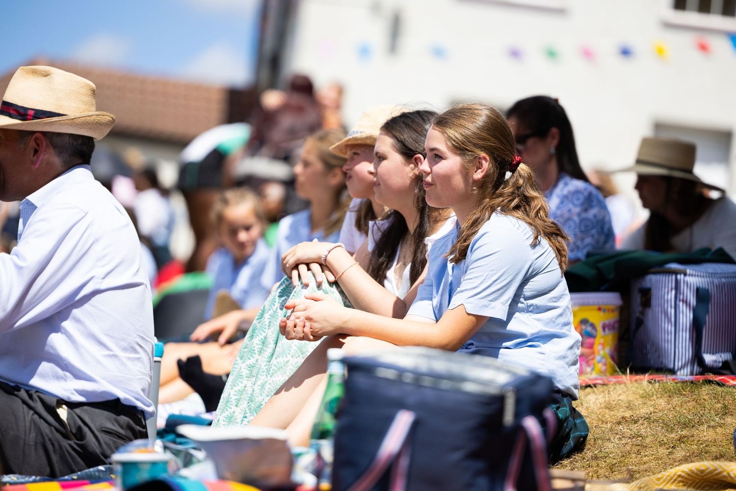 Outdoor gathering with people sitting on grass under bright blue sky.