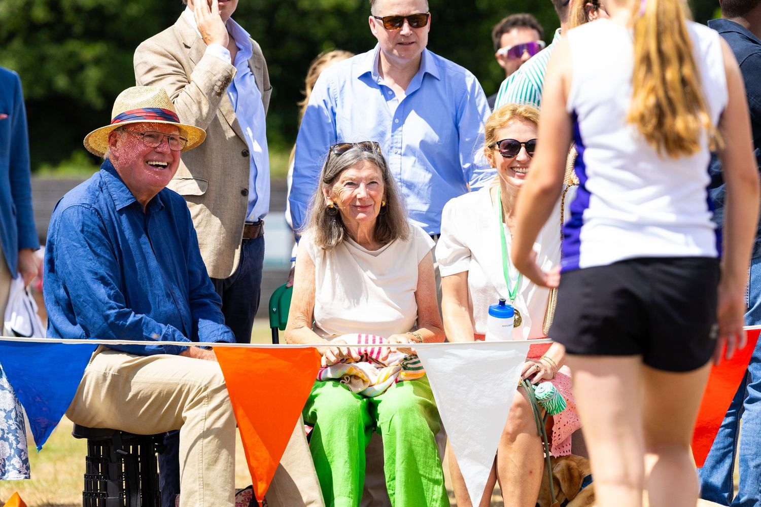 Spectators enjoy outdoor sporting event from sideline seating area on sunny summer day.