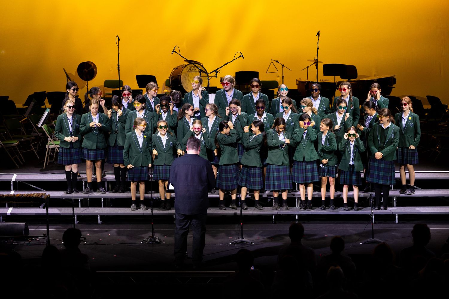 A silhouetted choir performs on a stage with dramatic golden lighting and black attire.