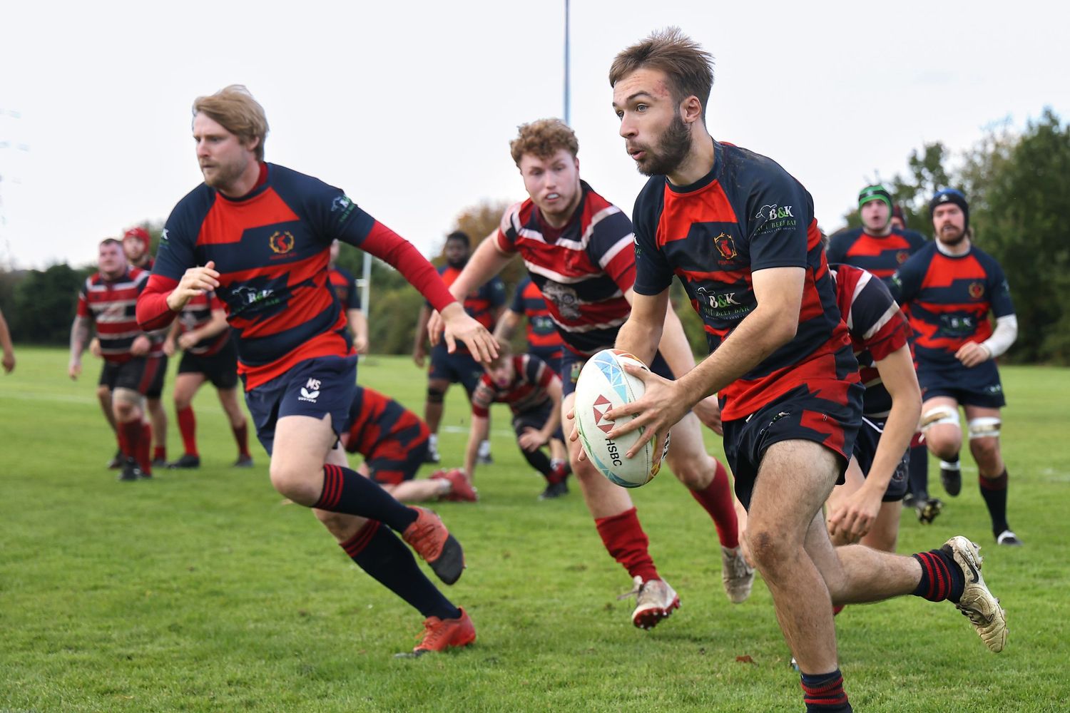 Rugby team in red and blue striped jerseys running with the ball during a match.