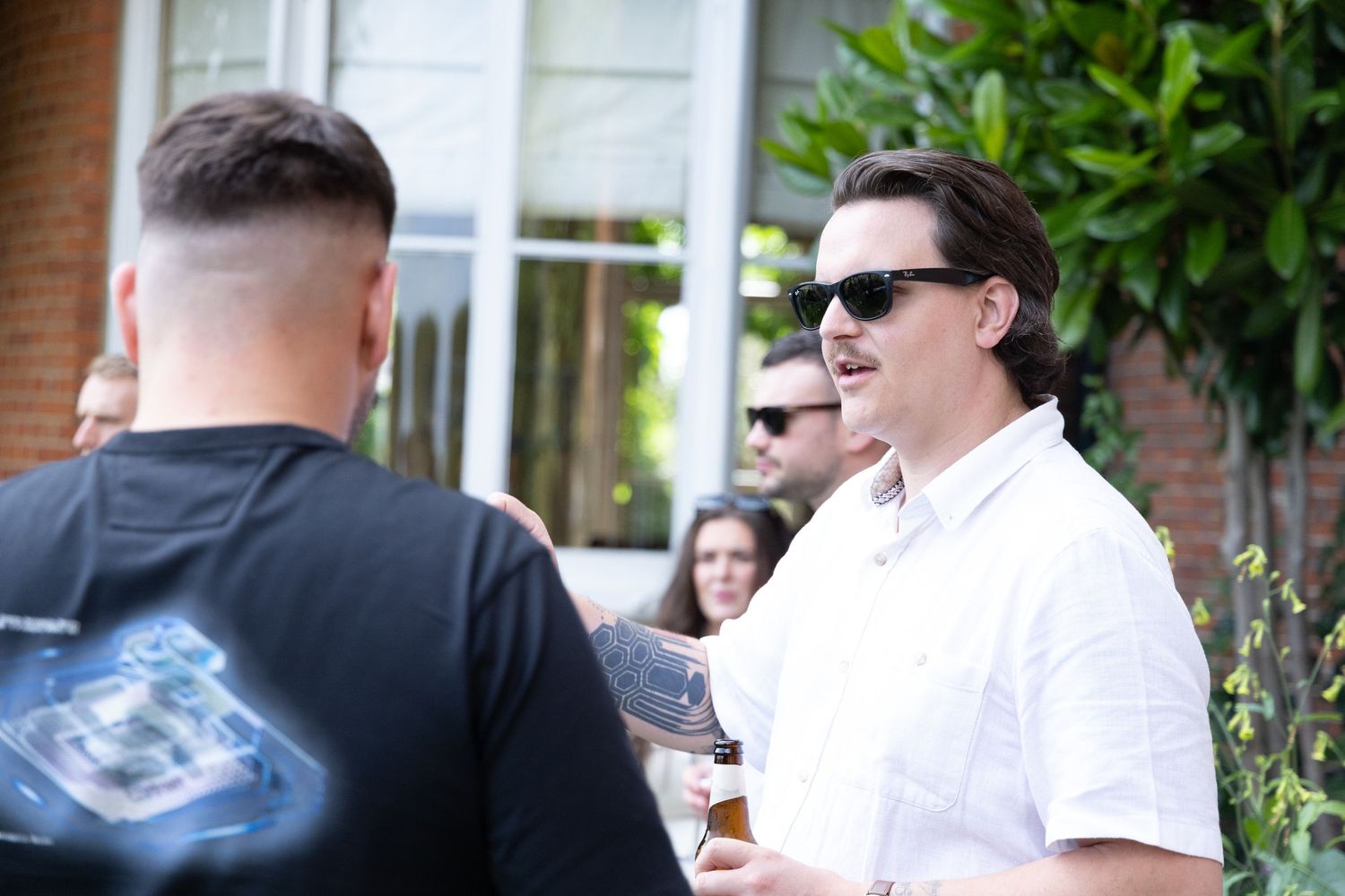 People socializing outdoors on a sunny day with drinks and casual attire.