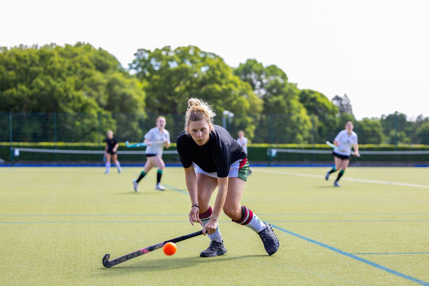 Field hockey player reaches low to make a diving stick save during an outdoor match on artificial turf field.