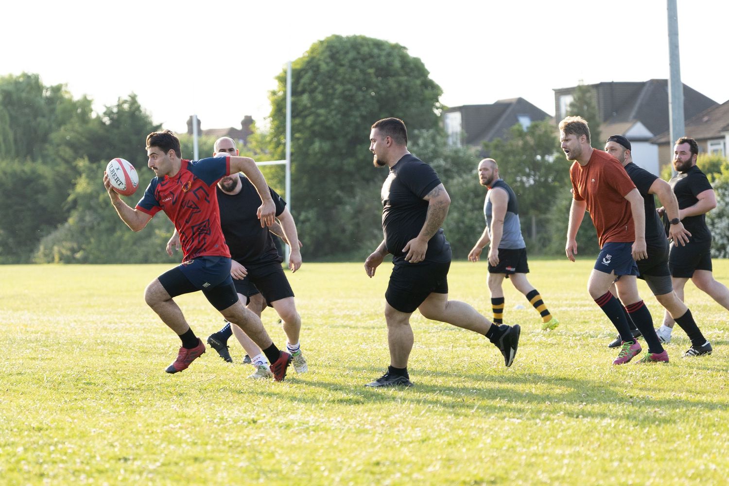 Rugby players competing for possession during a match at sunset on an open field.