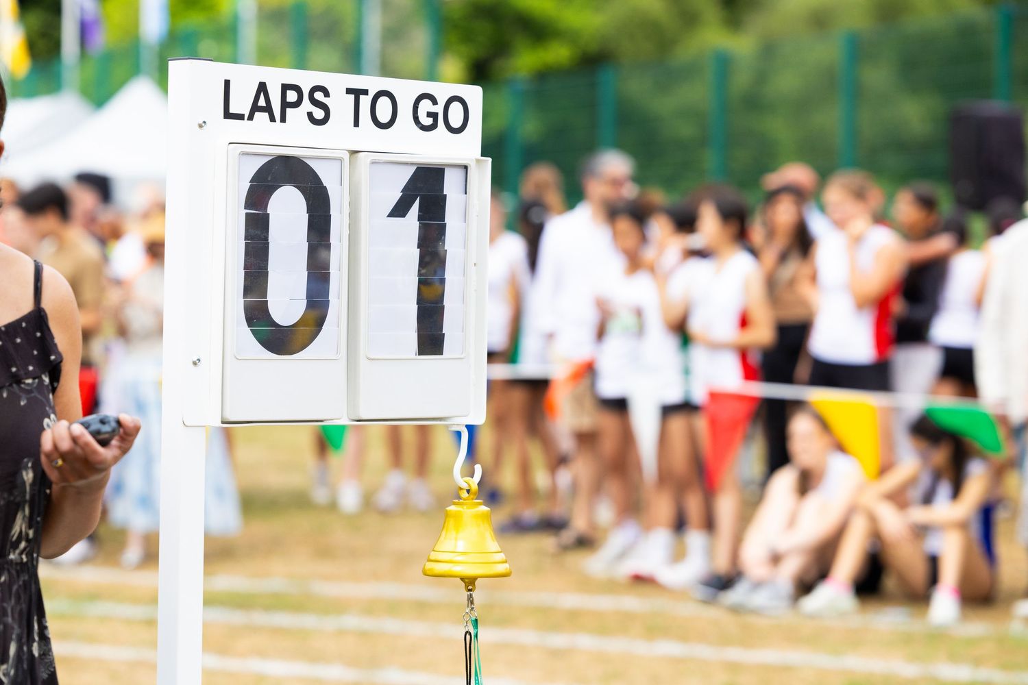 Race lap counter showing '01 LAPS TO GO' with blurred spectators in background at outdoor sporting event.