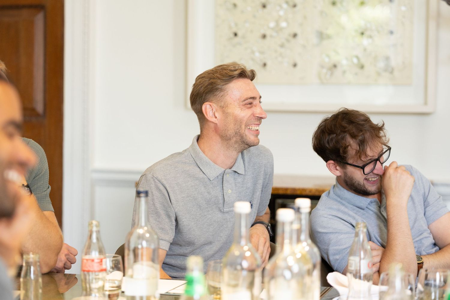 People in casual attire enjoying conversation at a dining table with drinks and bottles.