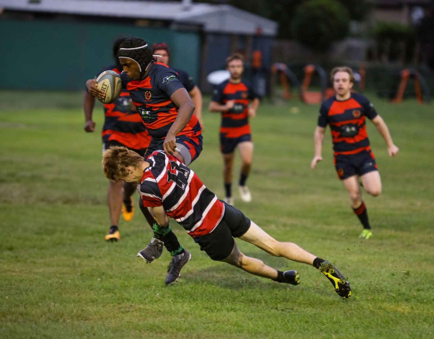 Rugby player making a diving tackle attempt during a match on a grass field.