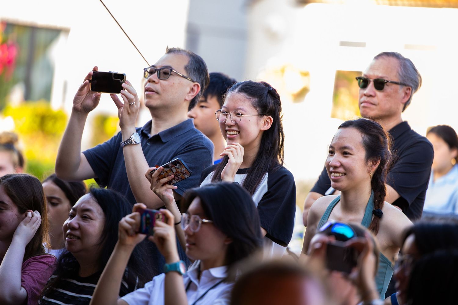 Excited crowd taking photos at outdoor event with phones and cameras.