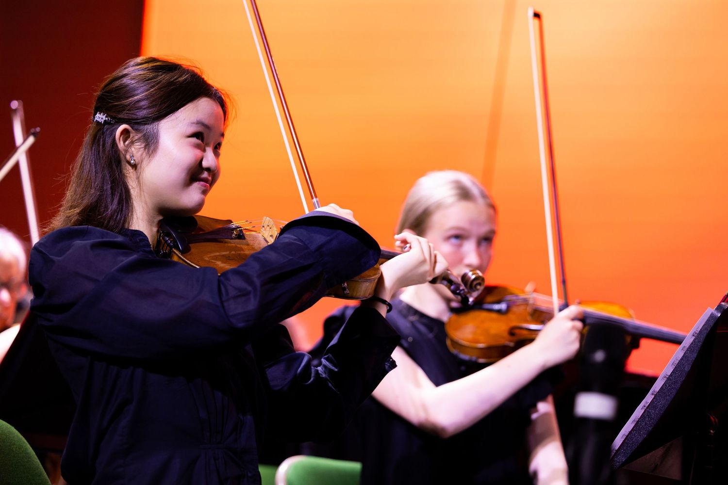 Musicians performing with string instruments against an orange backdrop.