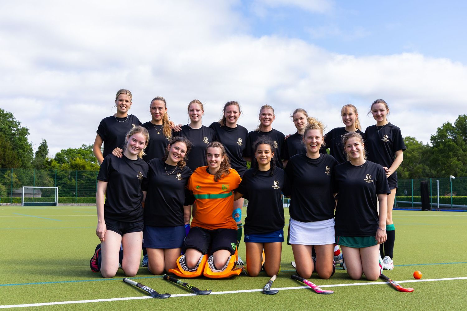 A sports team poses together on a sunny field with goal posts visible in the background.