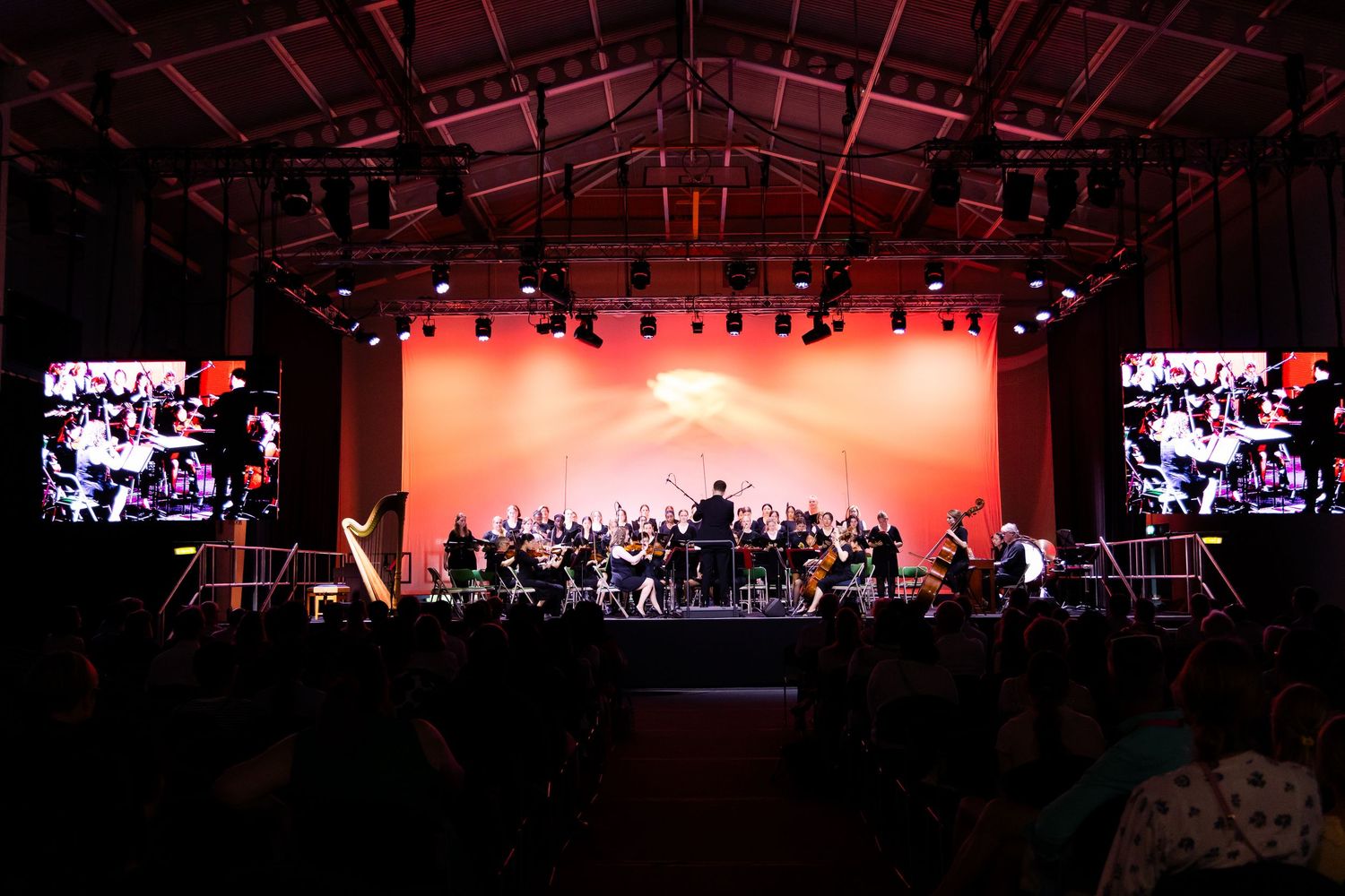 Wide view of concert stage with red lighting and silhouetted performers.