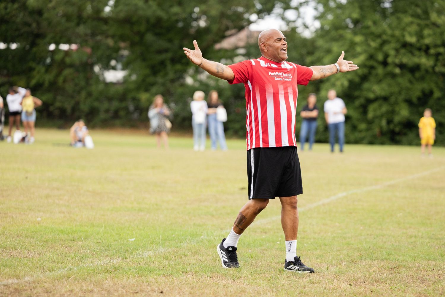 Athletes playing sports on a sunny grass field with spectators watching from the sidelines.