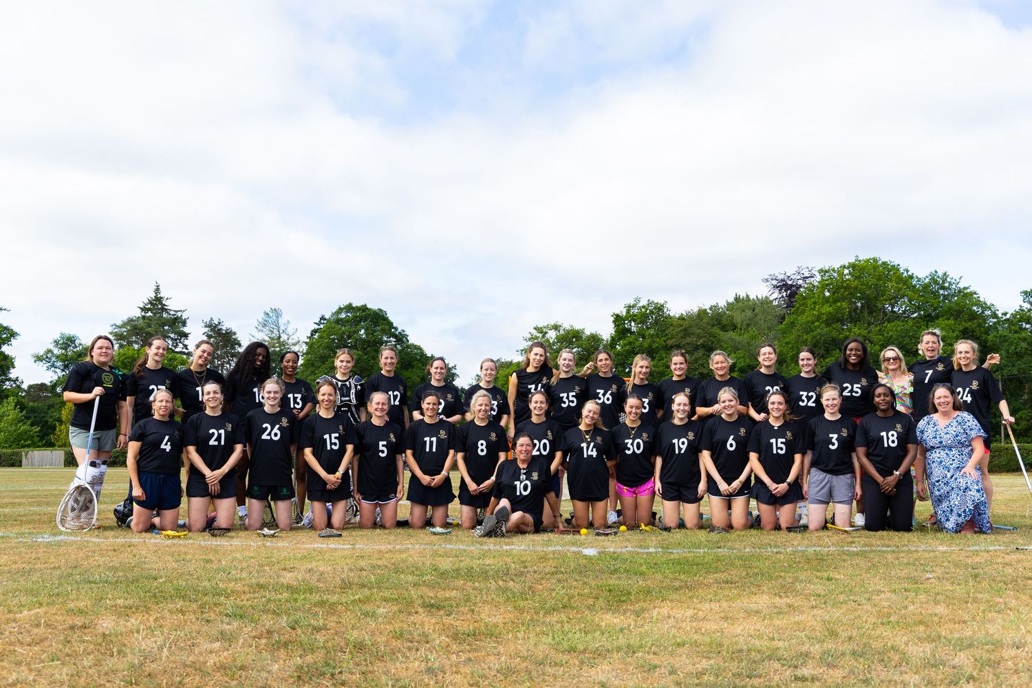 Large group of athletes in black uniforms posing together on a grassy field for a team photo.