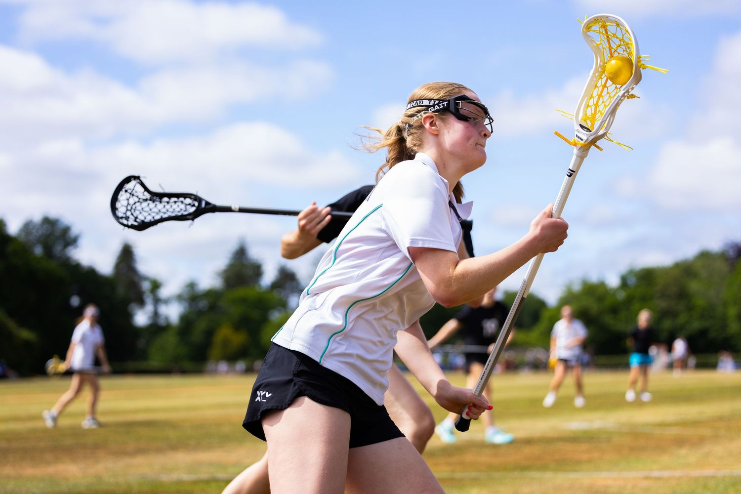 Lacrosse player runs with stick raised during outdoor game on grass field.