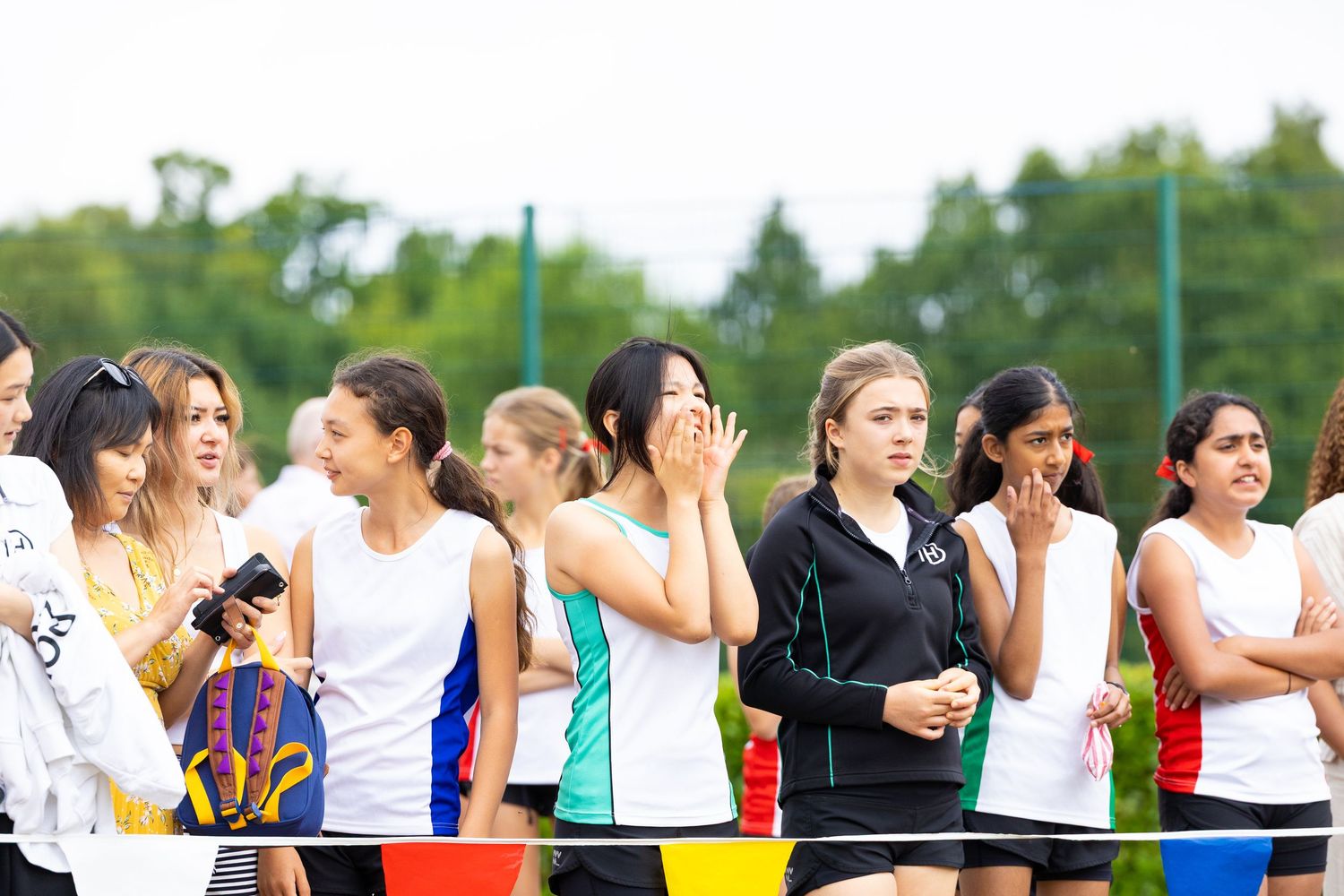 Athletes lined up at an outdoor track event waiting together on a grassy sports field.