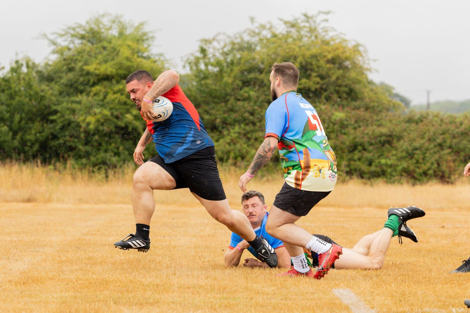 A flag football match in progress with players running on a dry grass field during a sunny day.