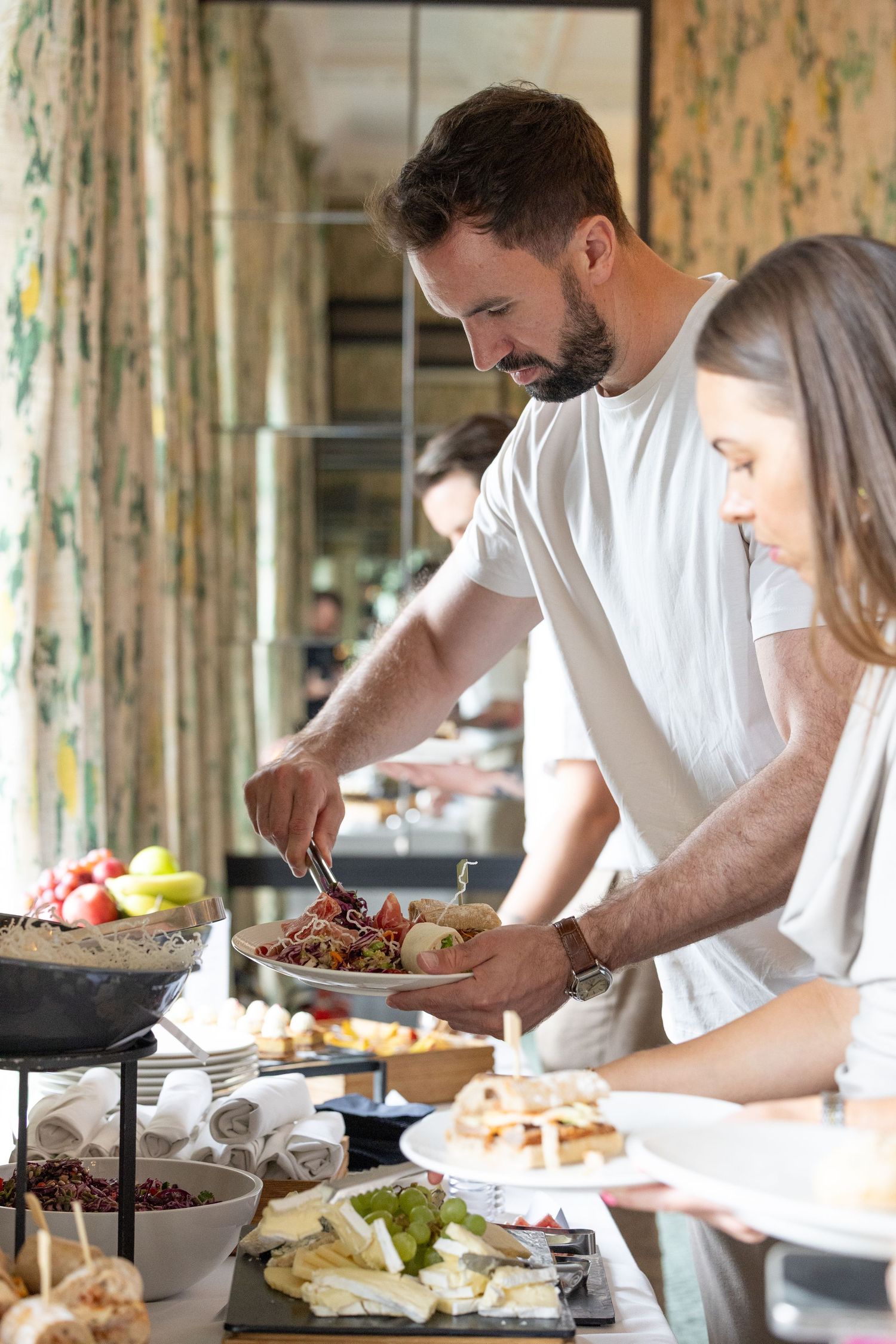 People preparing food at a buffet station with various dishes and appetizers spread across a table.