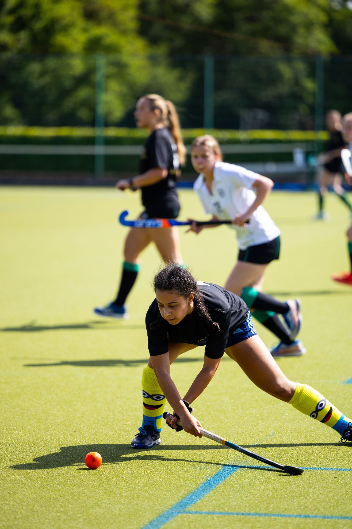 Field hockey player dribbles ball during intense match on artificial turf field.