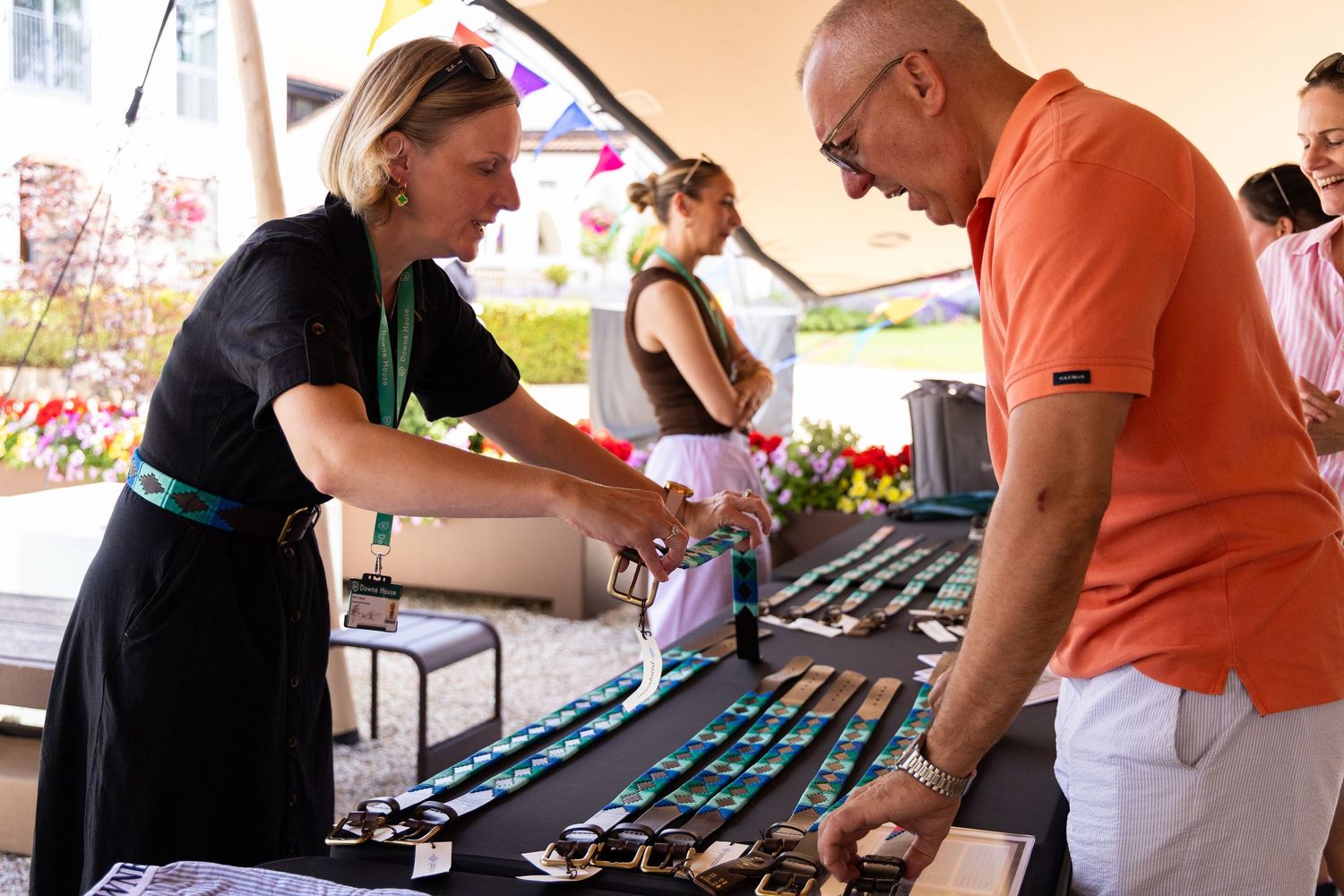 People examining items displayed on a long table at an outdoor festival or market event.