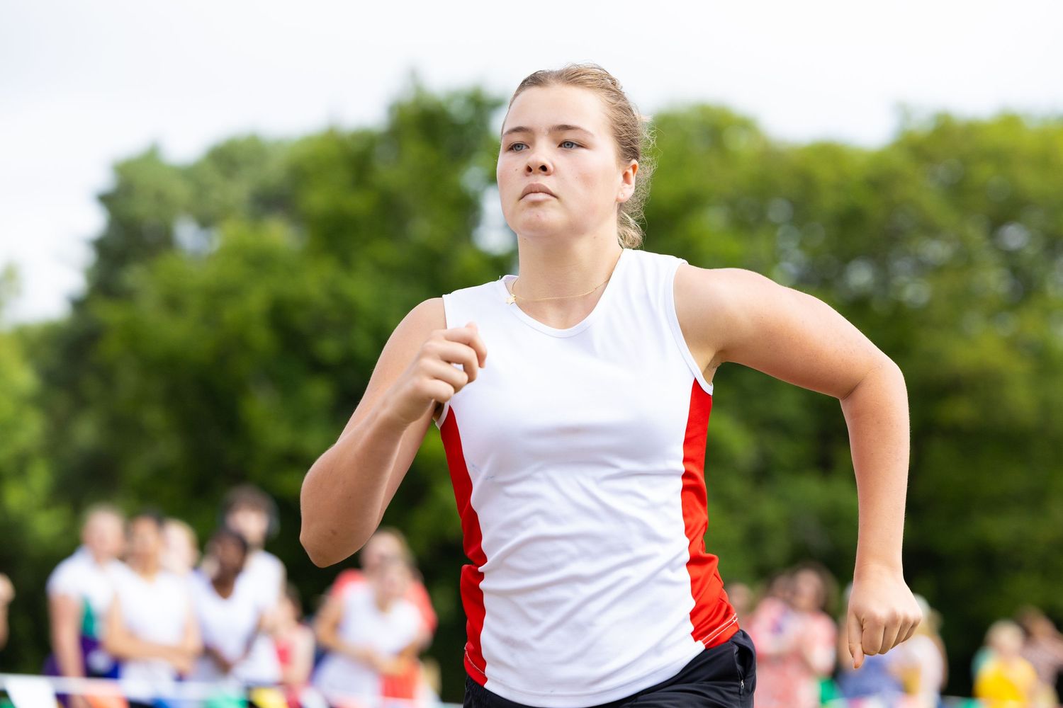 Athletes compete in a track and field event jumping over hurdles on a sunny day.