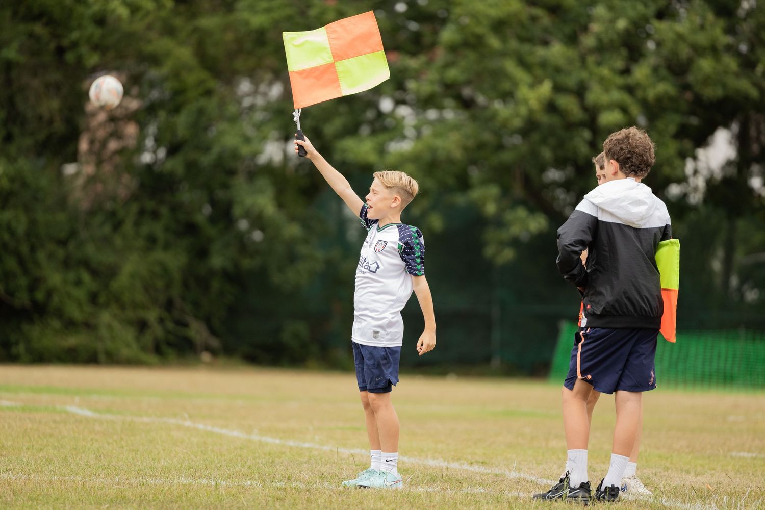 Young official raising a flag on the sideline of a sports field.