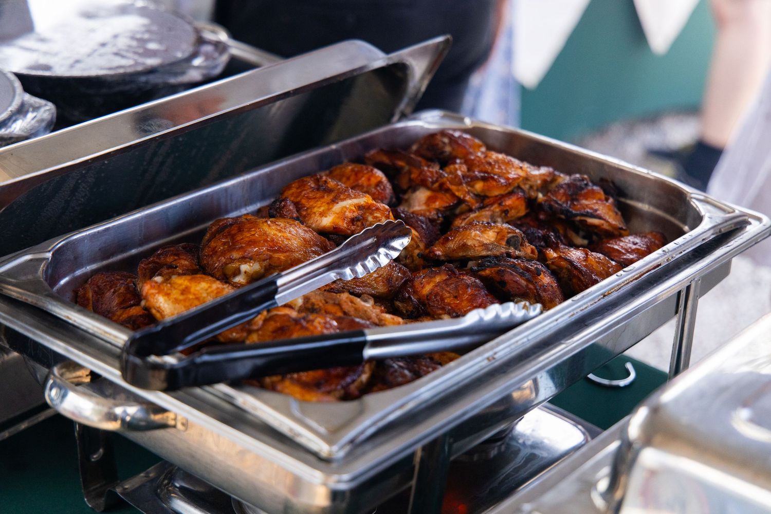 Rows of grilled chicken displayed in metal serving trays at a buffet.
